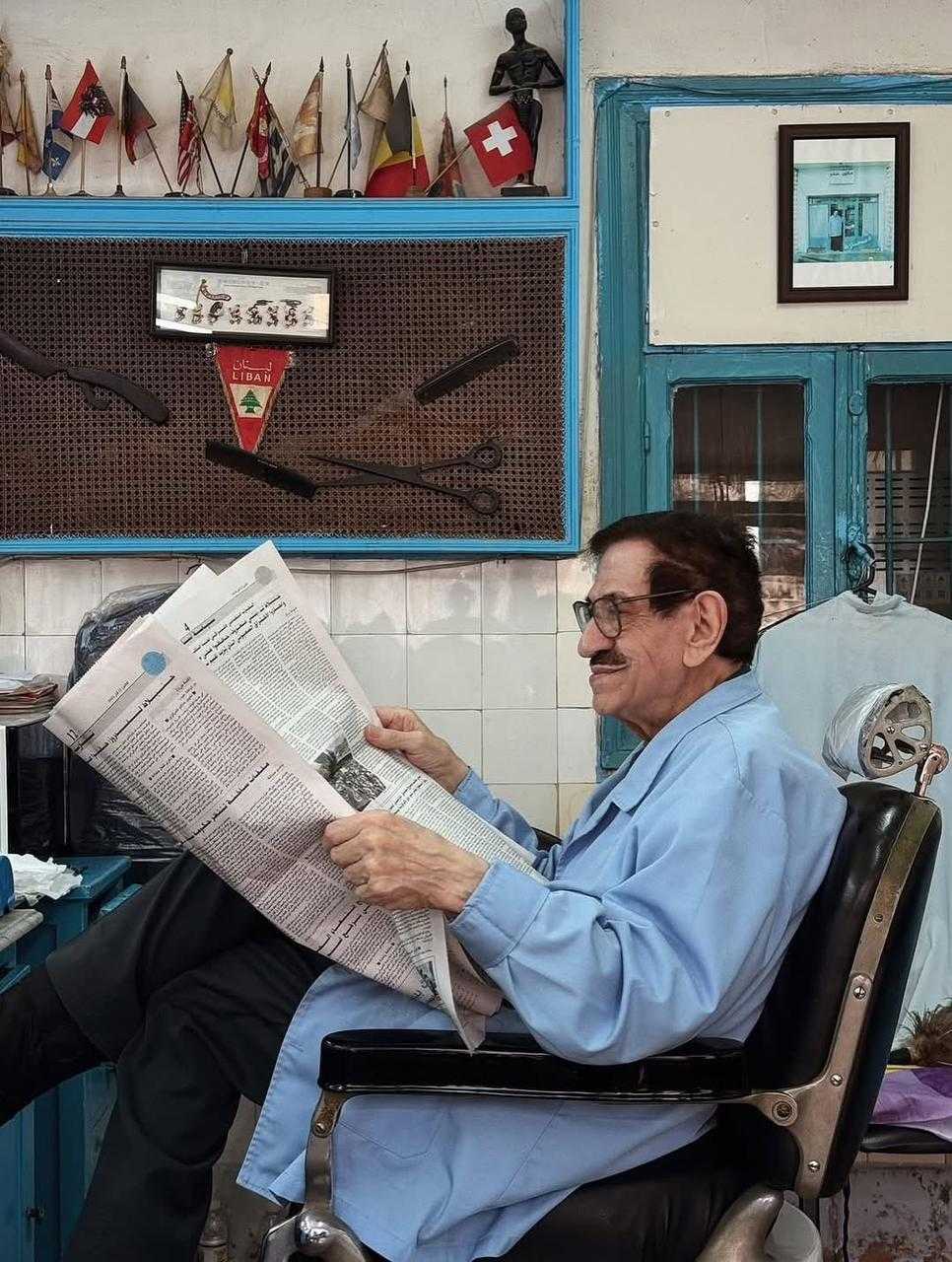An older Lebanese barber sits comfortably on his chair in his shop
