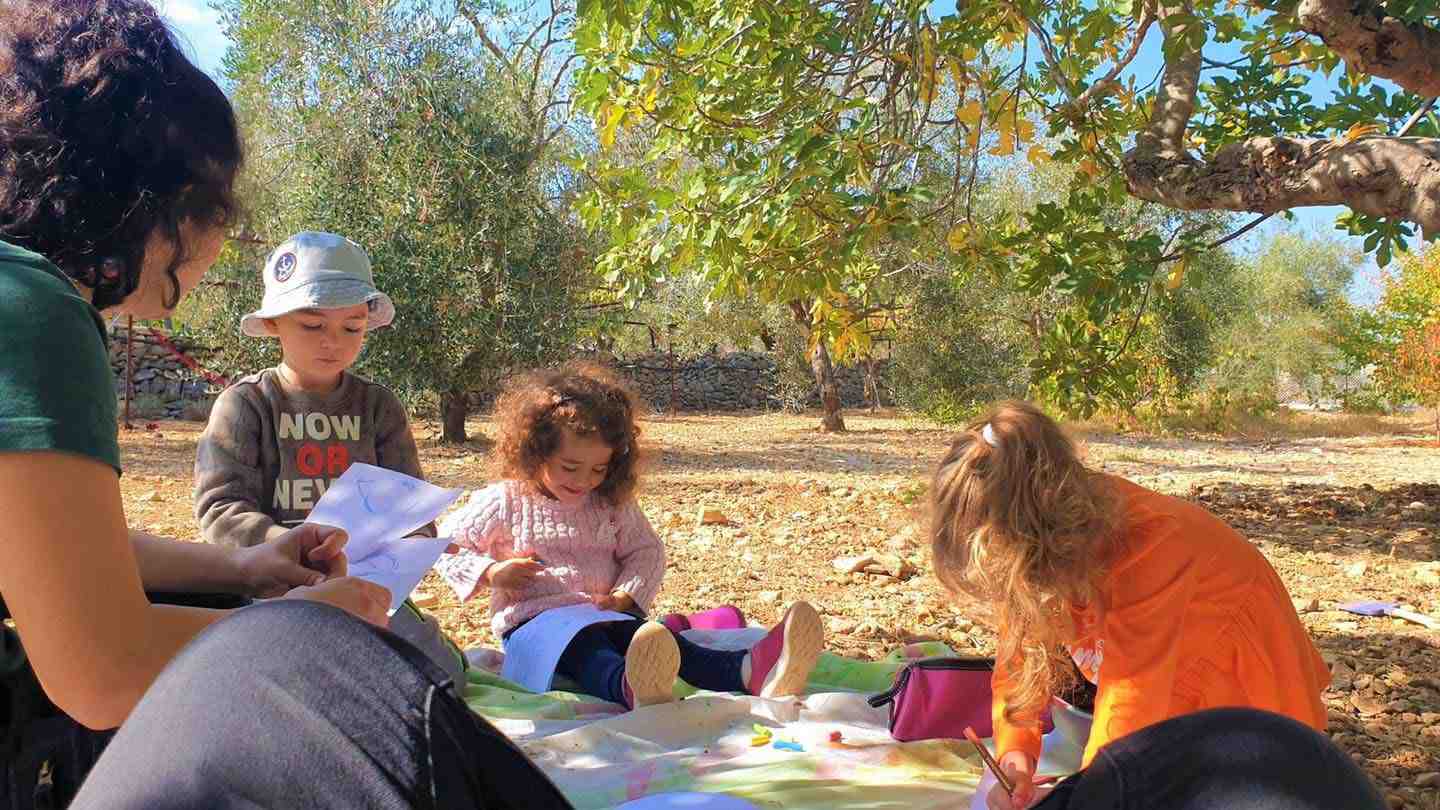 Children sitting on a colorful blanket, deeply focused on their drawings.