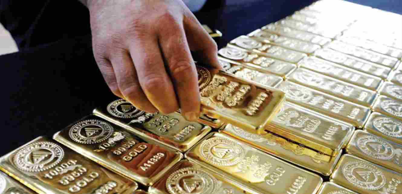 Hand holding a gold bar over stacked bullion